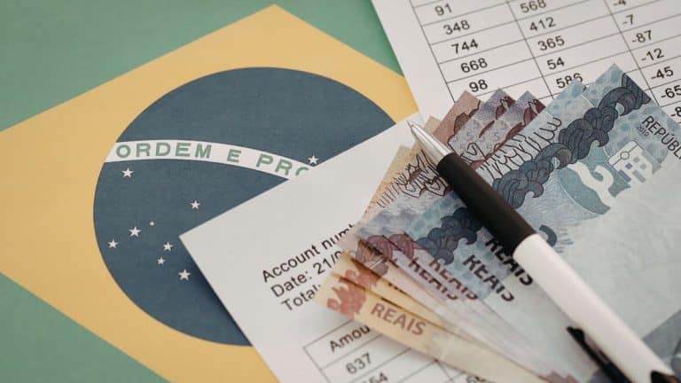 Cédulas de real, caneta e documentos sobre a bandeira do Brasil ilustram pagamentos e valores do INSS
