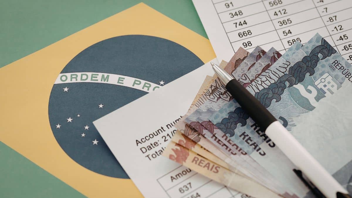 Cédulas de real, caneta e documentos sobre a bandeira do Brasil ilustram pagamentos e valores do INSS