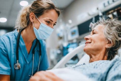 Profissional de enfermagem presta cuidados a paciente idosa em ambiente hospitalar.