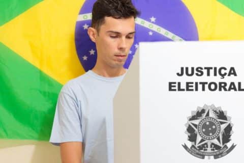 Eleitor vota em urna da Justiça Eleitoral com bandeira do Brasil ao fundo, imagem ilustrativa sobre ano eleitoral e mudanças no governo federal