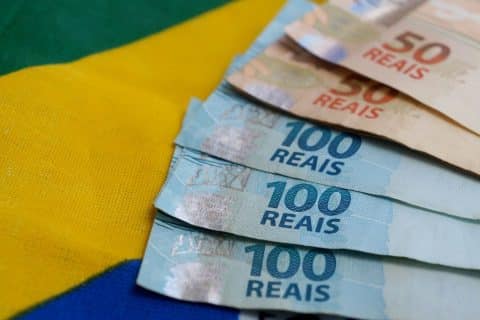 Cédulas de real sobre a bandeira do Brasil ilustram mudanças nas regras do PIS/Pasep em 2026