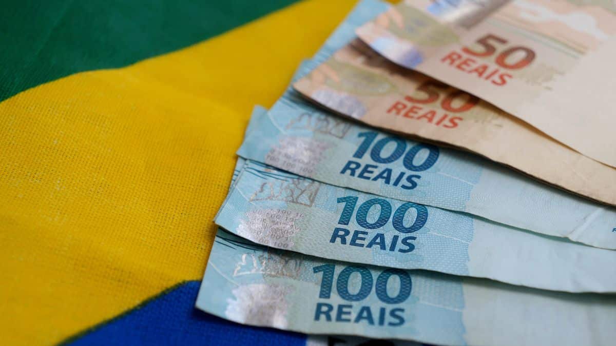 Cédulas de real sobre a bandeira do Brasil ilustram mudanças nas regras do PIS/Pasep em 2026